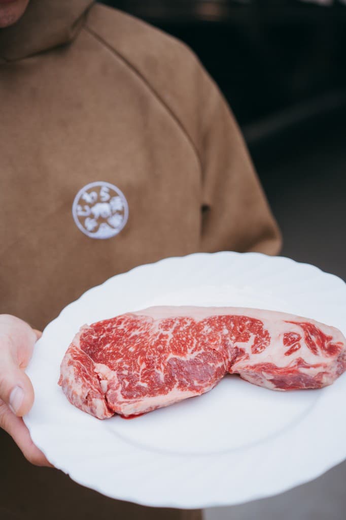 白い皿に載せた霜降りの牛肉塊を、両手で前に差し出すスタッフ